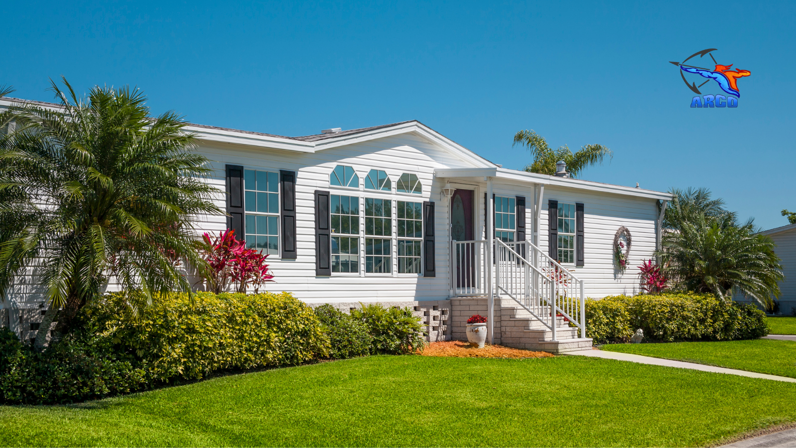 A anchored mobile home is sitting on top of a lush green lawn in a residential area.