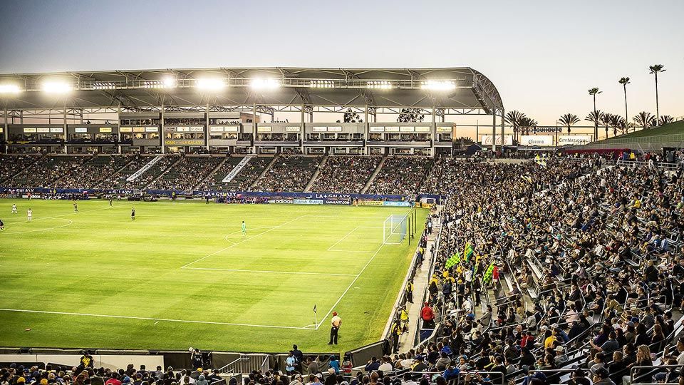 Soccer stadium filled with cheering fans, illuminated field under lights, evening.