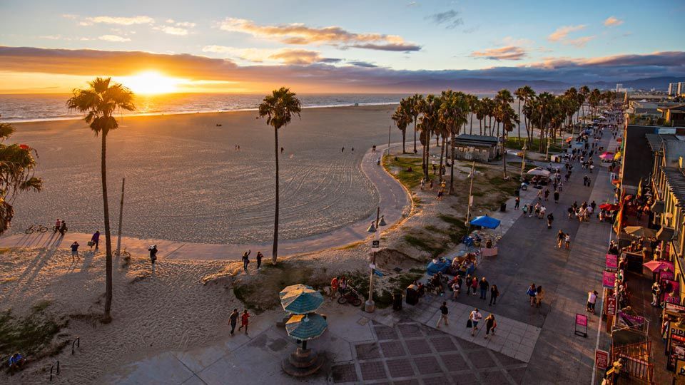 Sunset over Venice Beach, California; palm trees, people, sand, and boardwalk.
