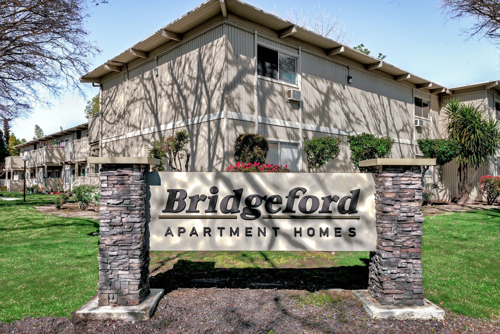 Sign for Bridgeford Apartment Homes in front of a two-story apartment building with trees.