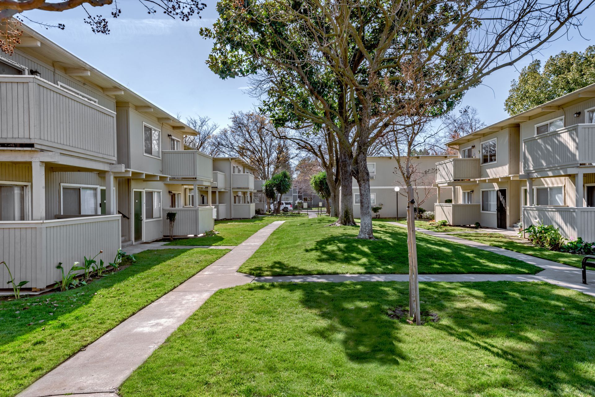 Row of beige apartment buildings with balconies and a grassy walkway.