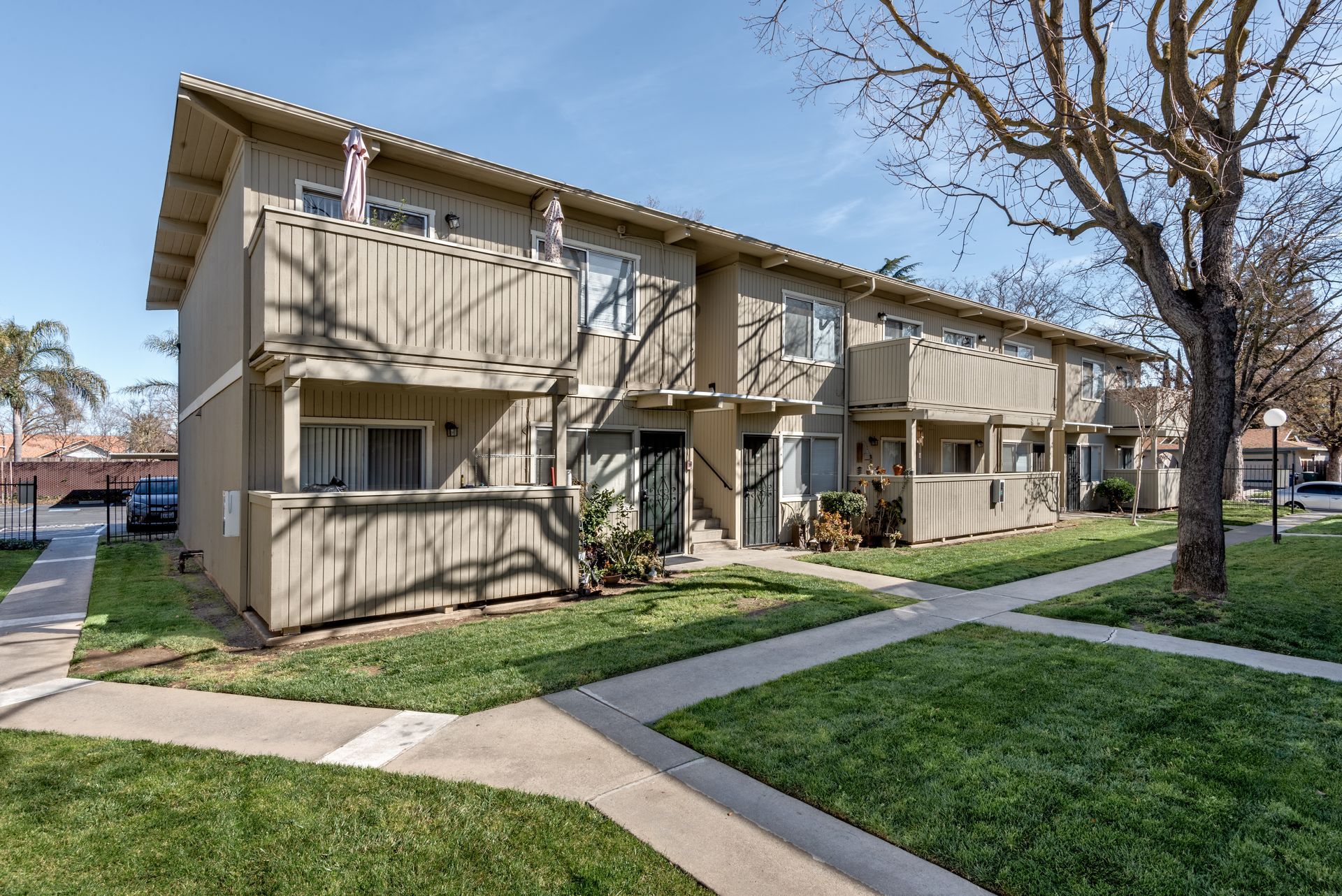Beige two-story townhomes with green grass and sidewalks under a clear blue sky.