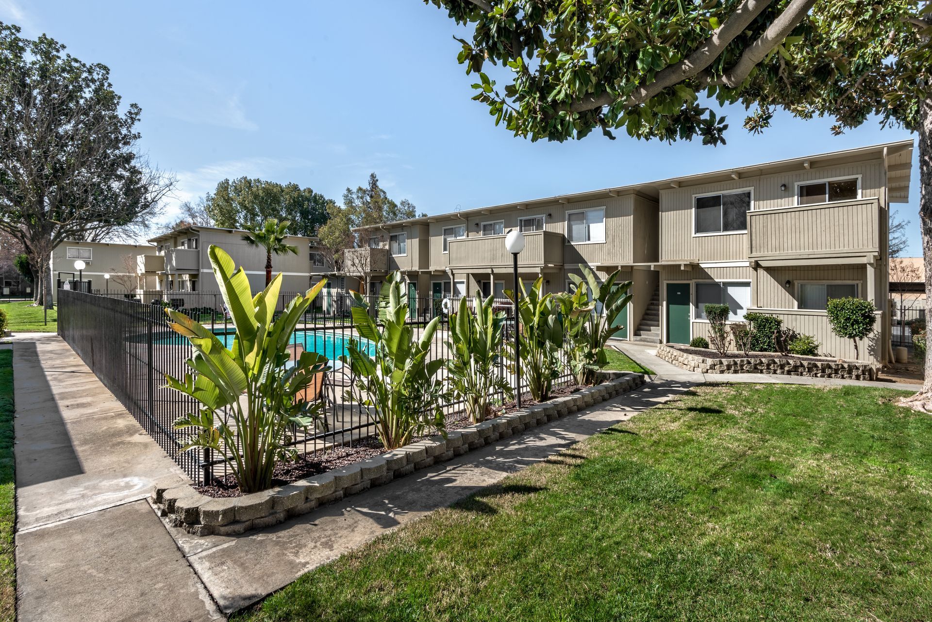 Apartment building with a pool and lawn, sunny day.