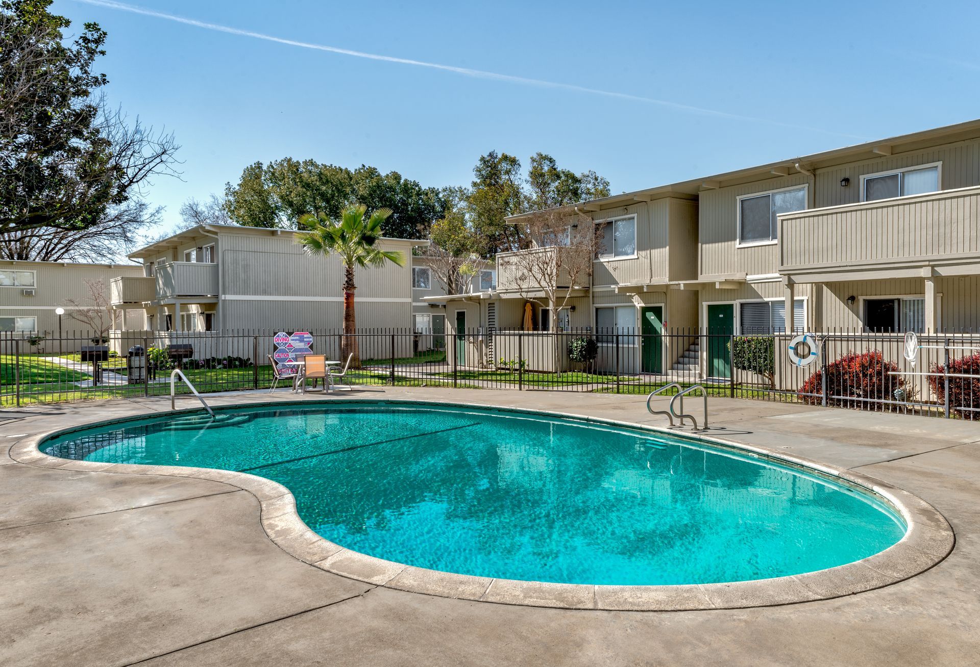 Apartment complex with a swimming pool. Tan buildings, green pool, blue sky.