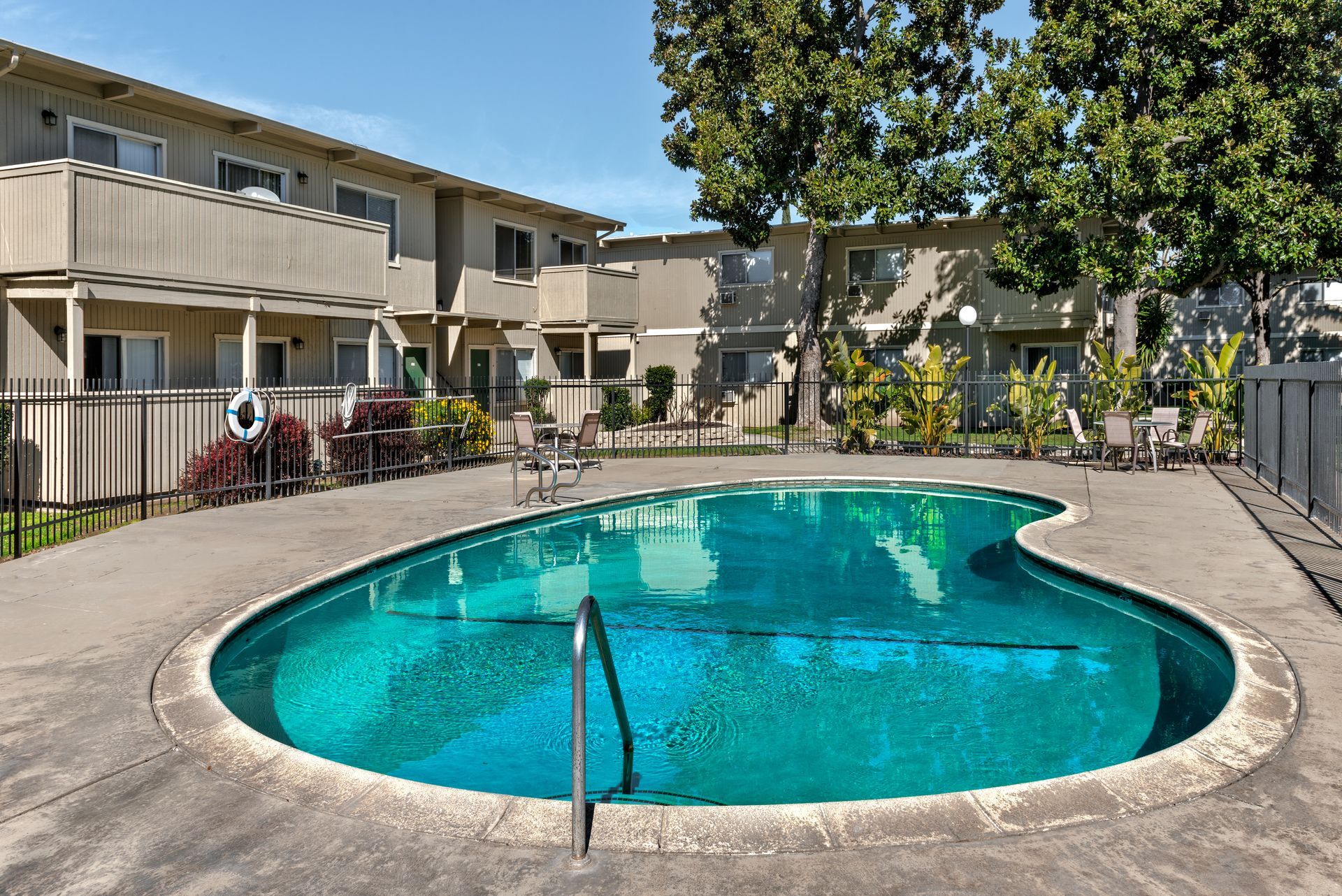 Apartment complex with a turquoise-colored, kidney-shaped swimming pool surrounded by concrete.