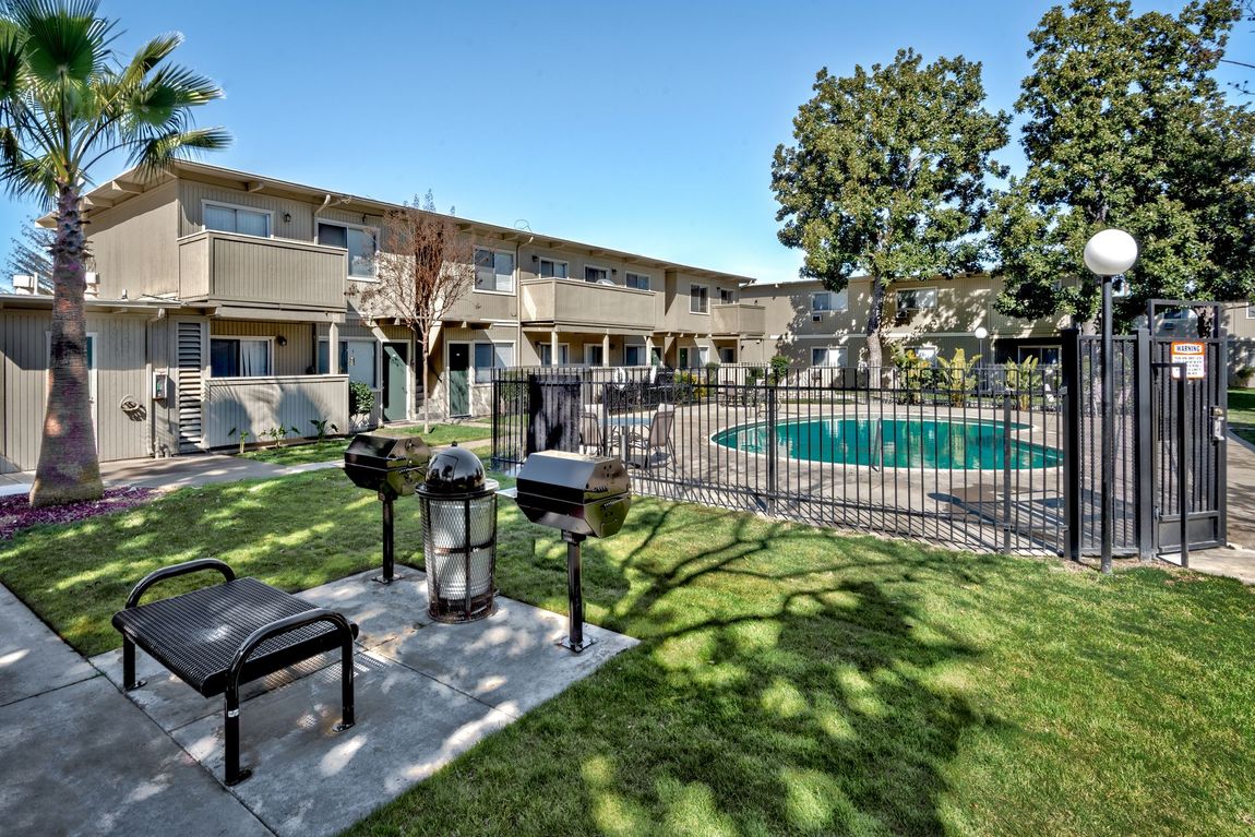 Apartment complex with a pool, grills, and seating on a sunny day.