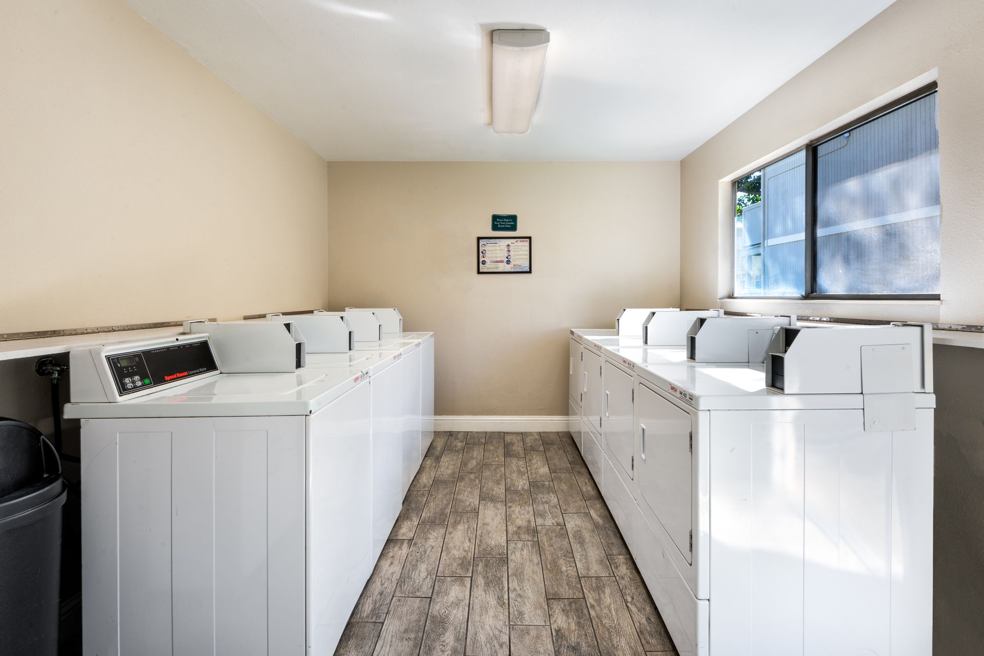 Laundry room with white washers, a window, and a trash can.