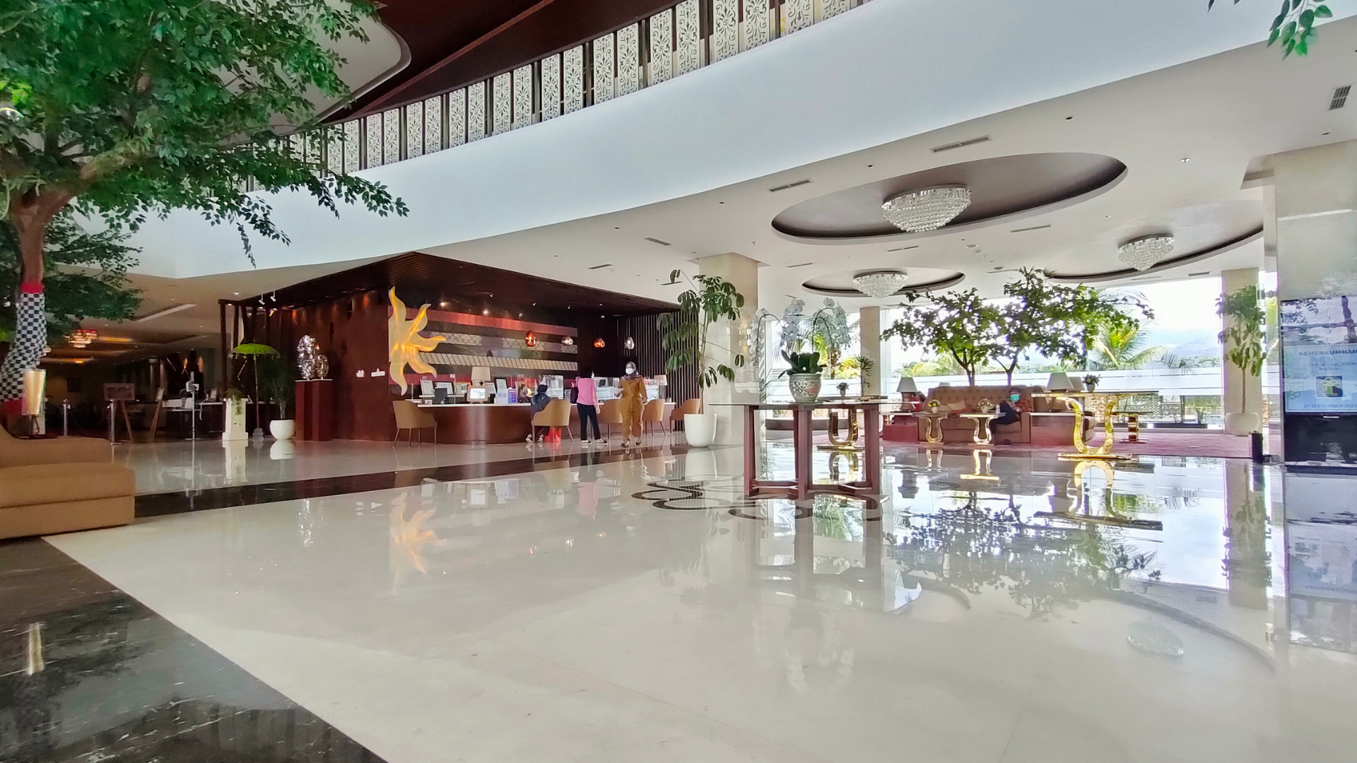 Hotel lobby with polished floors and reception desk; trees and seating areas are visible.