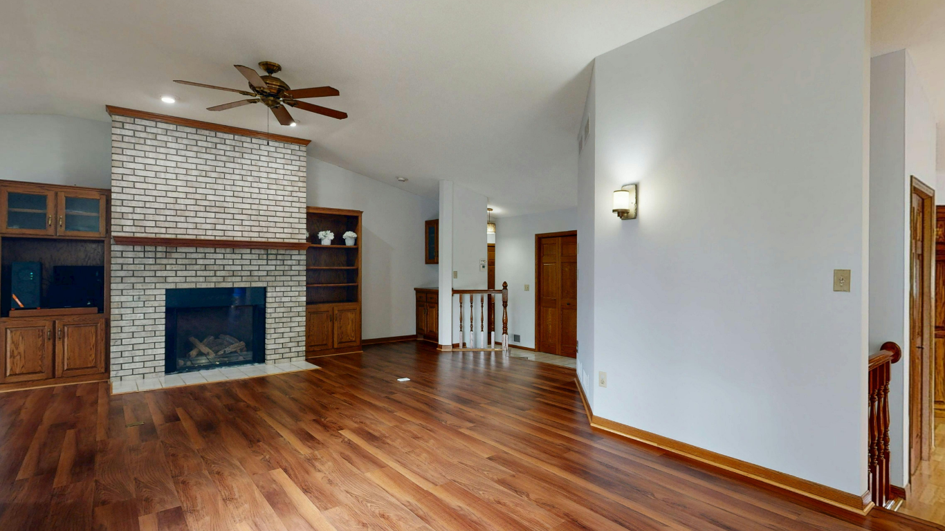 Living room with a patterned fireplace, wooden cabinets, hardwood floors, and a ceiling fan.