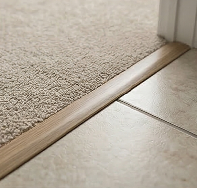 A wooden transition strip bridges the gap between beige carpet and light-colored tile flooring in a doorway.