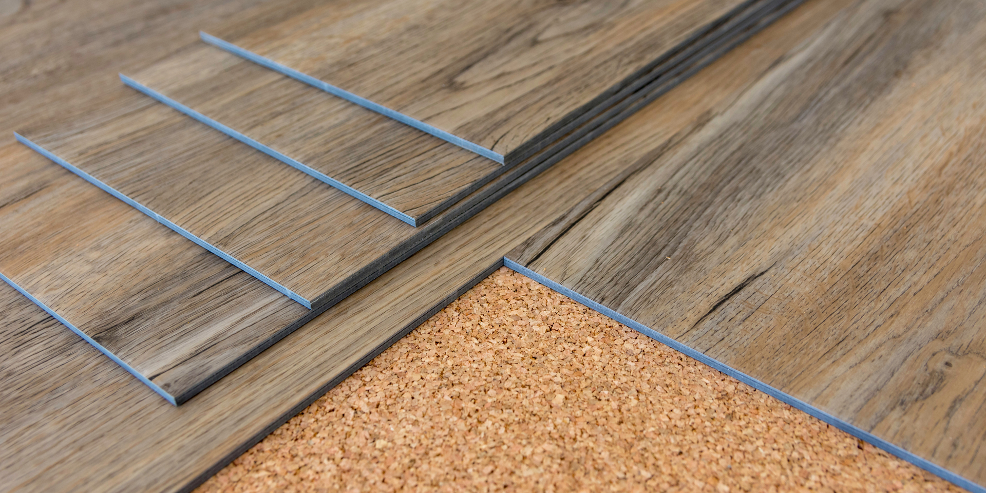 Several planks of wood-look luxury vinyl flooring stacked over a layer of brown cork underlayment.
