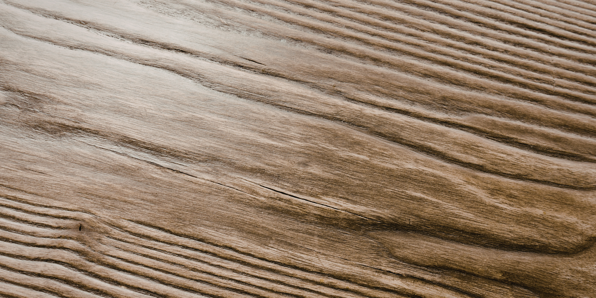 Close-up of rippled, brown sandy surface with subtle, wavy patterns and varying textures created by wind or water.