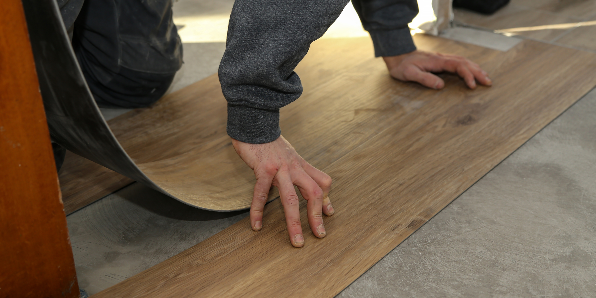 A person installing wood-look vinyl plank flooring on a concrete subfloor.