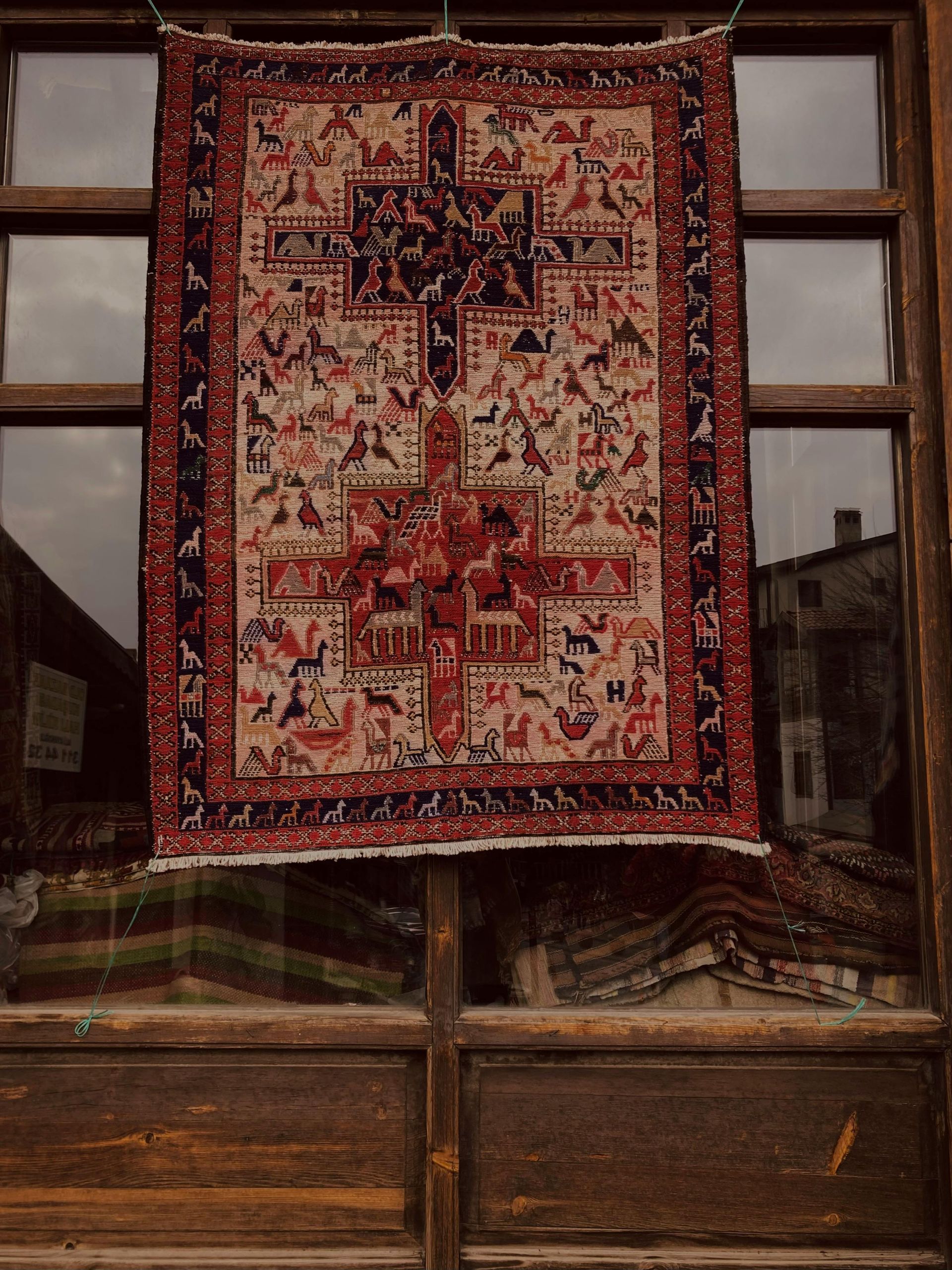 A decorative rug with red, white, and black cross patterns hanging in a window frame.