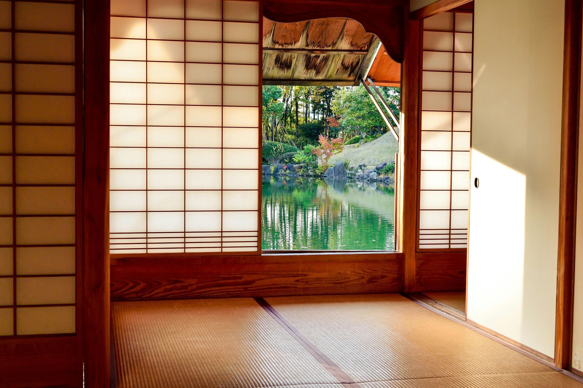 A traditional Japanese room with tatami flooring and shoji screens overlooking a serene pond and lush greenery.