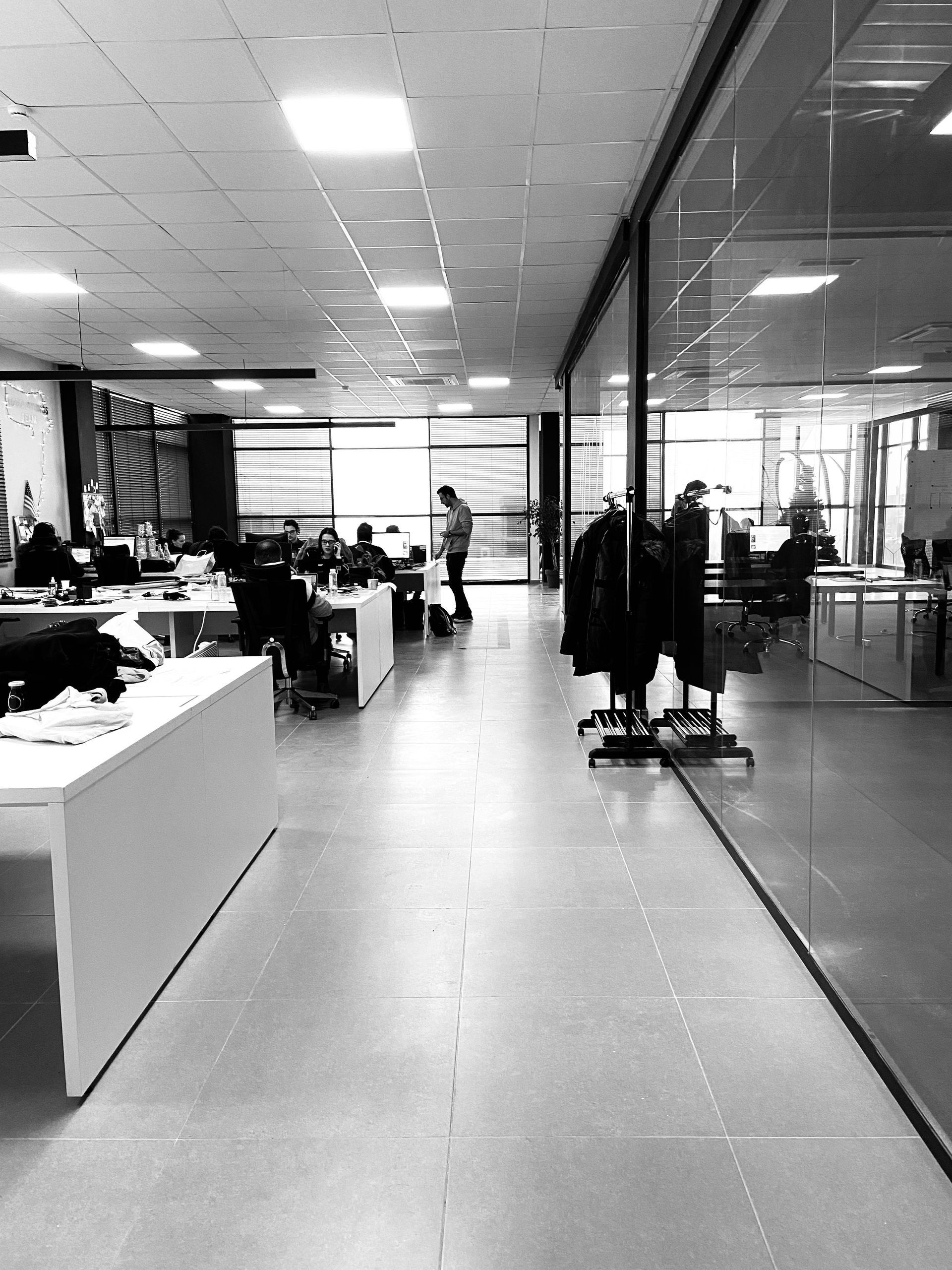 A black-and-white view of a modern office with desks, people working, and a glass-walled conference room.