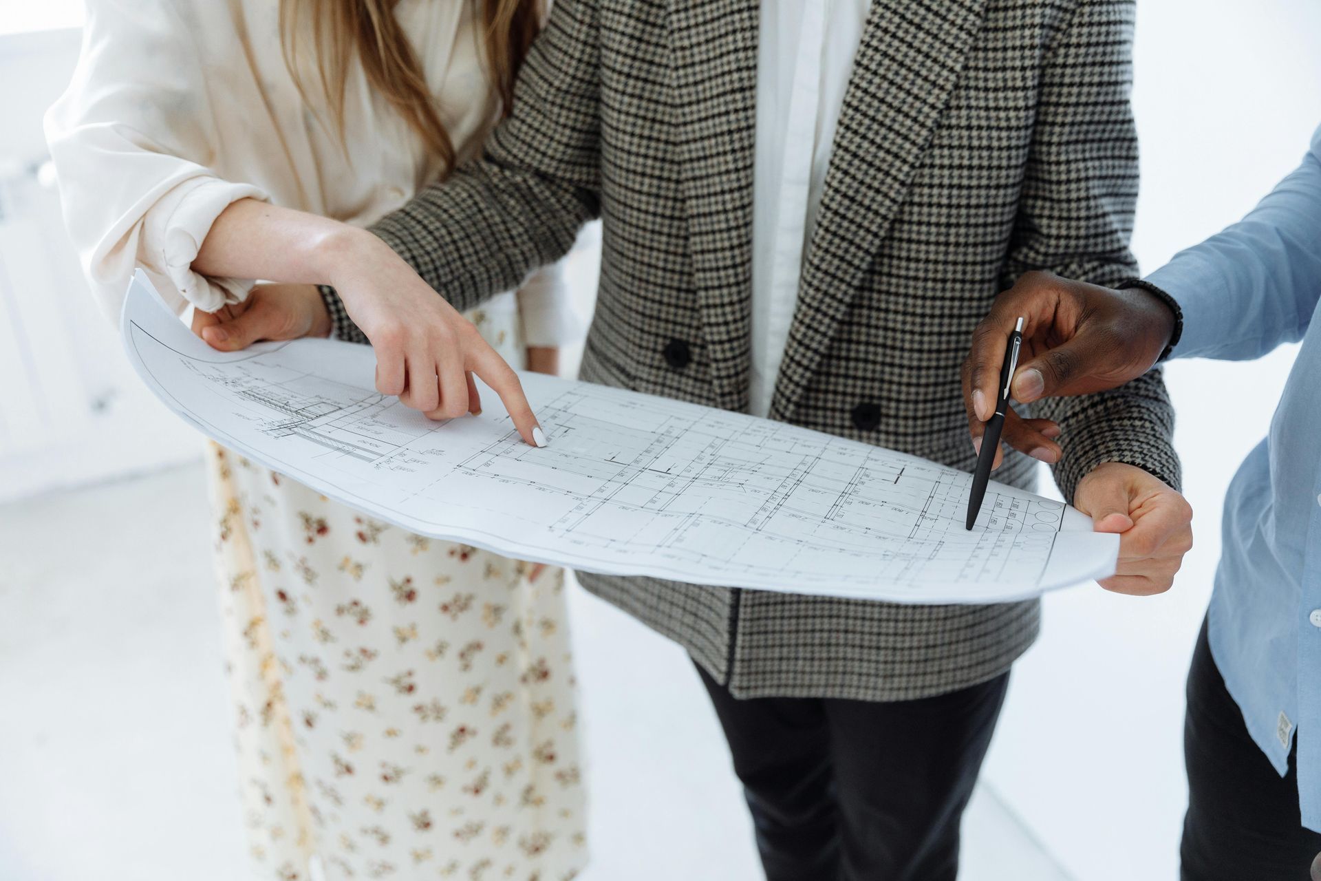Three people in professional attire gather around a large white blueprint, pointing at details as they review the plans.