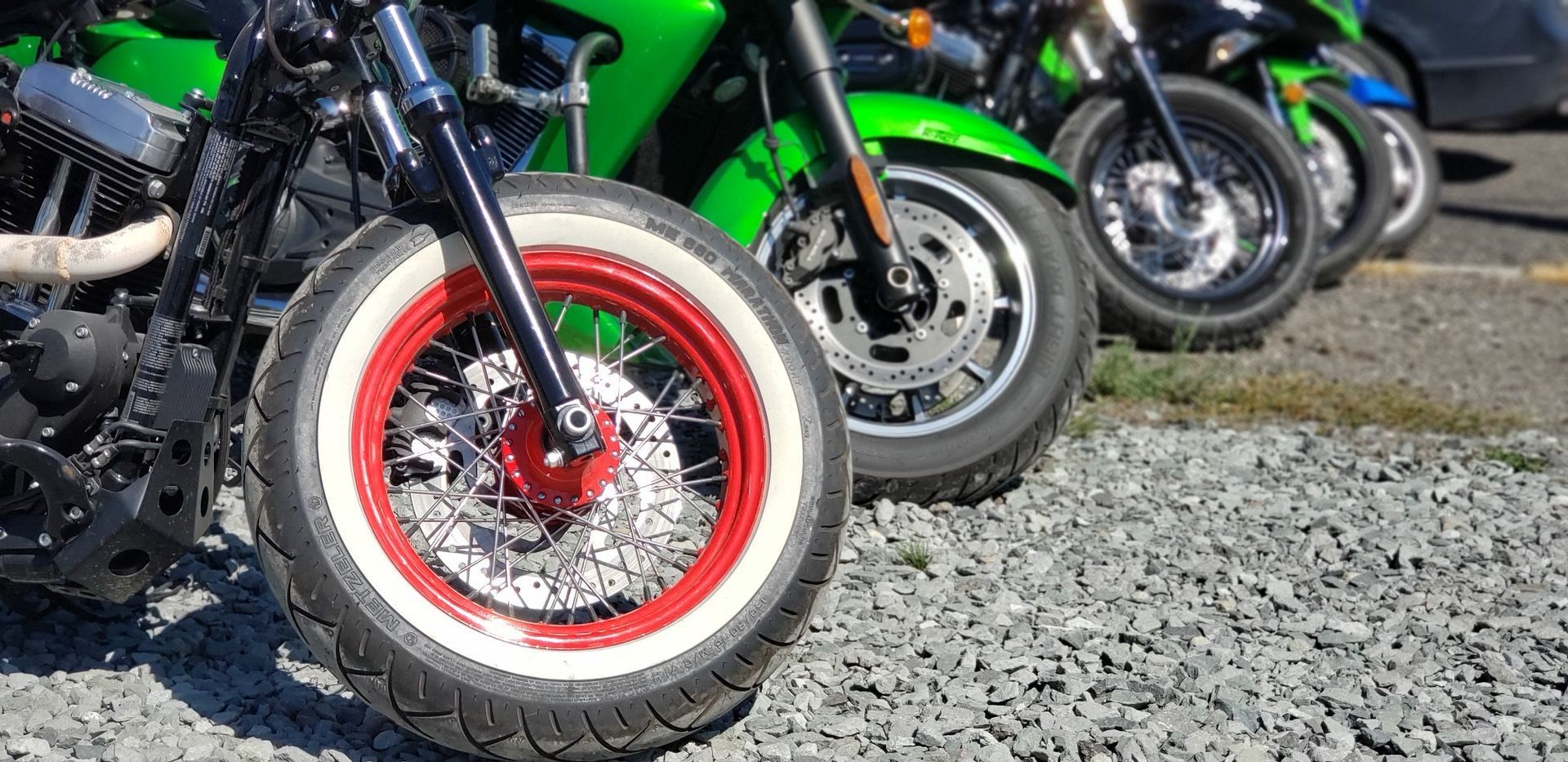 A row of motorcycles are parked in a gravel lot.