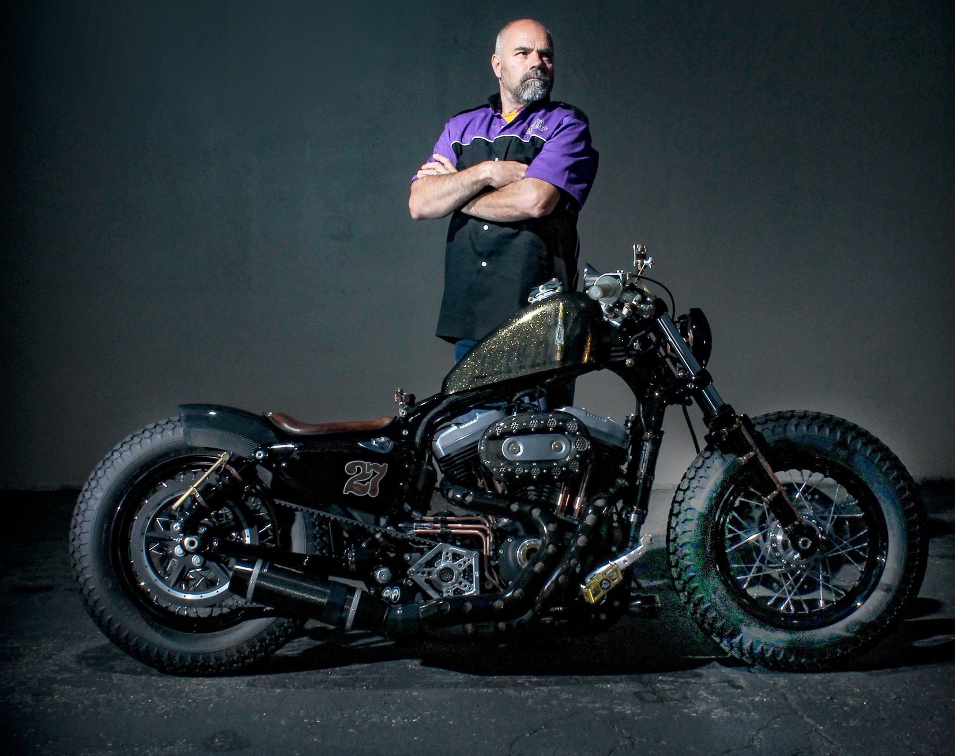 A man in a purple shirt is standing next to a motorcycle