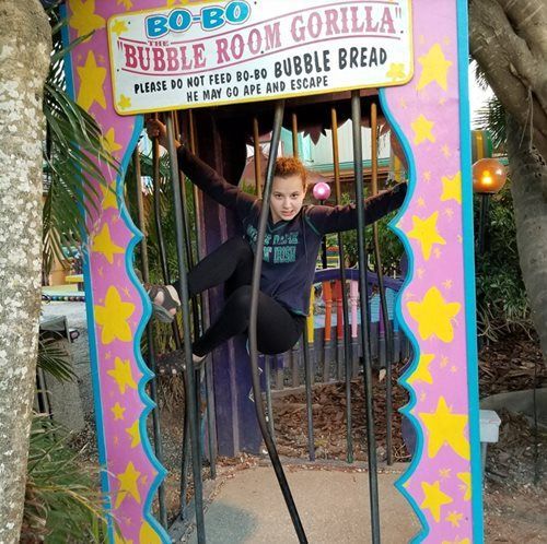 A person climbs through a bent metal bar of a pink, star-decorated cage labeled