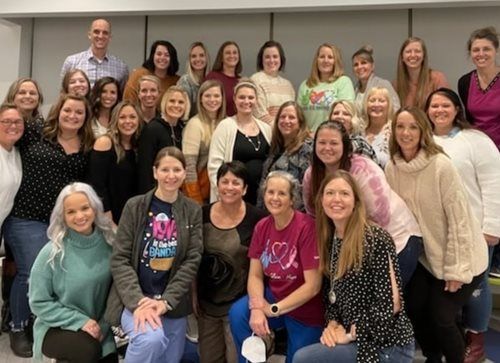 A large group of people smiling and posing for a photo in an indoor setting with neutral walls.