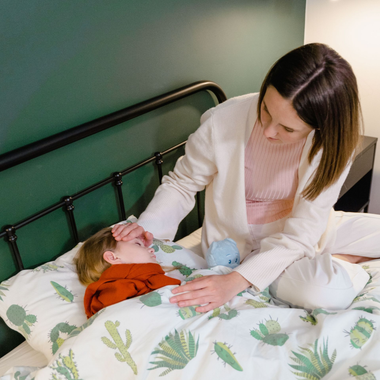Woman tending to a sick child in bed with a green wall and patterned bedding