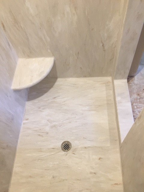 A shower stall with a drain and a shelf in a bathroom.