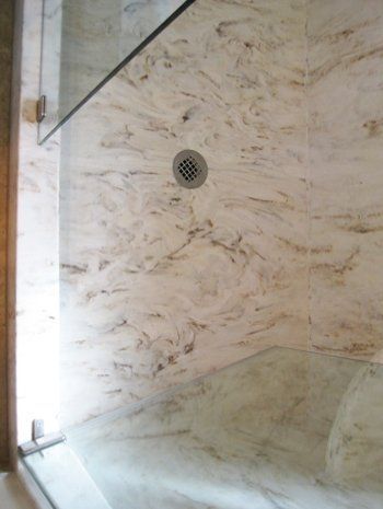 A shower with a drain on the floor and a marble wall.