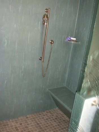 A shower with a stainless steel shower head and a bench.