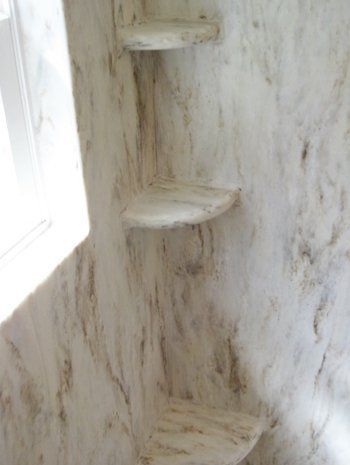 A bathroom with marble walls and shelves in the corner.