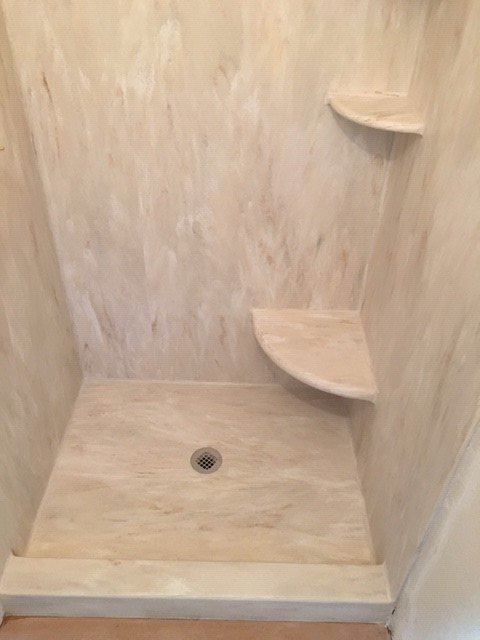 A shower stall with a drain and shelves in a bathroom.