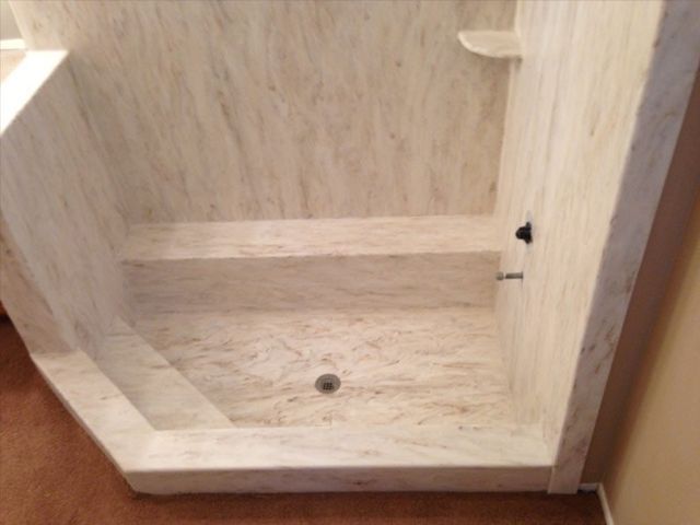A shower stall in a bathroom with a marble wall and floor.
