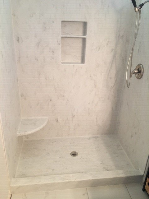 A shower stall with a shelf and a shower head in a bathroom.
