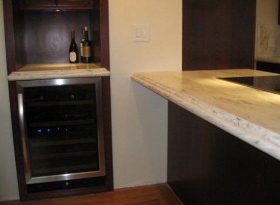 A bottle of wine sits on a counter next to a wine cooler