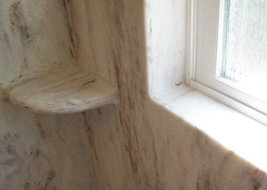 A bathroom with a marble shower wall and a window.