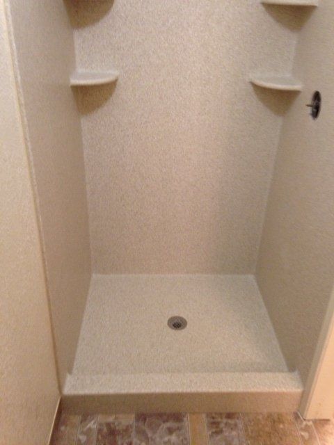 A shower stall with a drain and shelves in a bathroom.