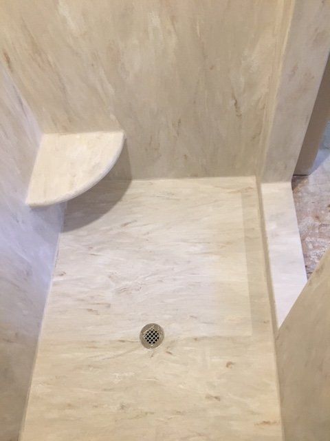 A shower stall with a drain and a shelf in a bathroom.