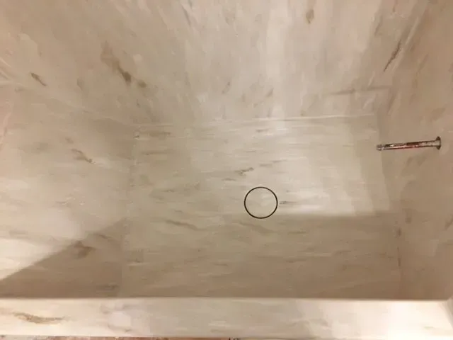 A shower stall with a drain hole in the floor.
