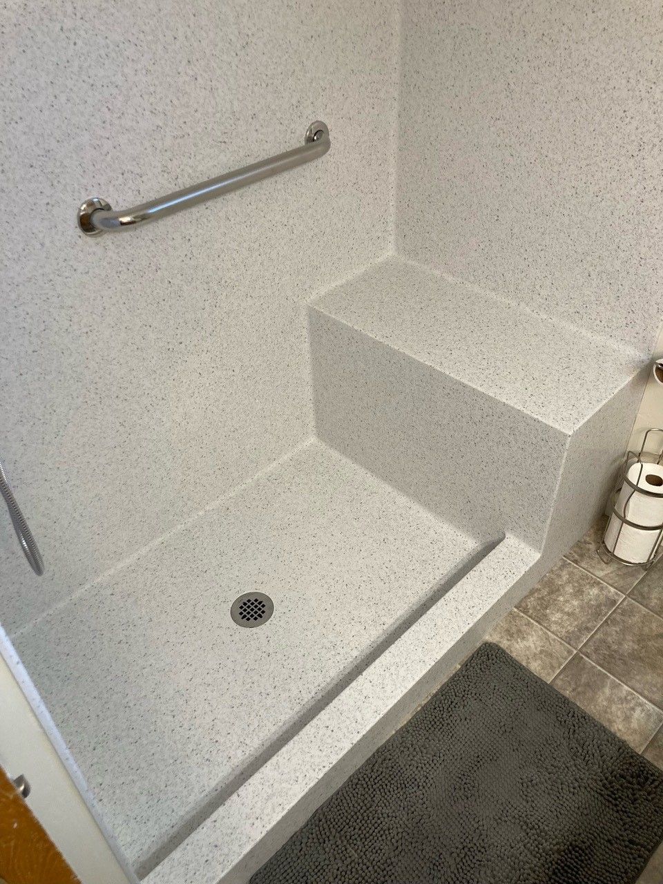 A bathroom with a walk in shower with a seat and a hand rail.