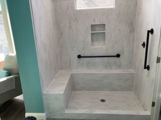 A bathroom with a walk in shower with a seat and a hand rail.
