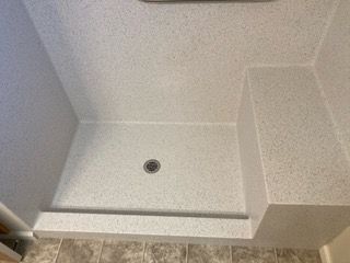 A shower stall with a seat and a drain in a bathroom.