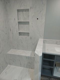 A bathroom with marble walls , a sink , a shower and a mirror.