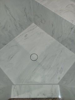 A white marble shower with a circle in the middle of it.