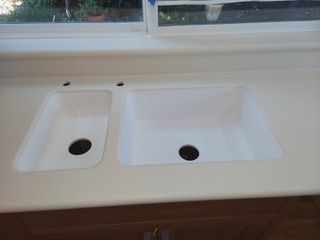 A kitchen sink with two holes in it is sitting on a counter next to a window.
