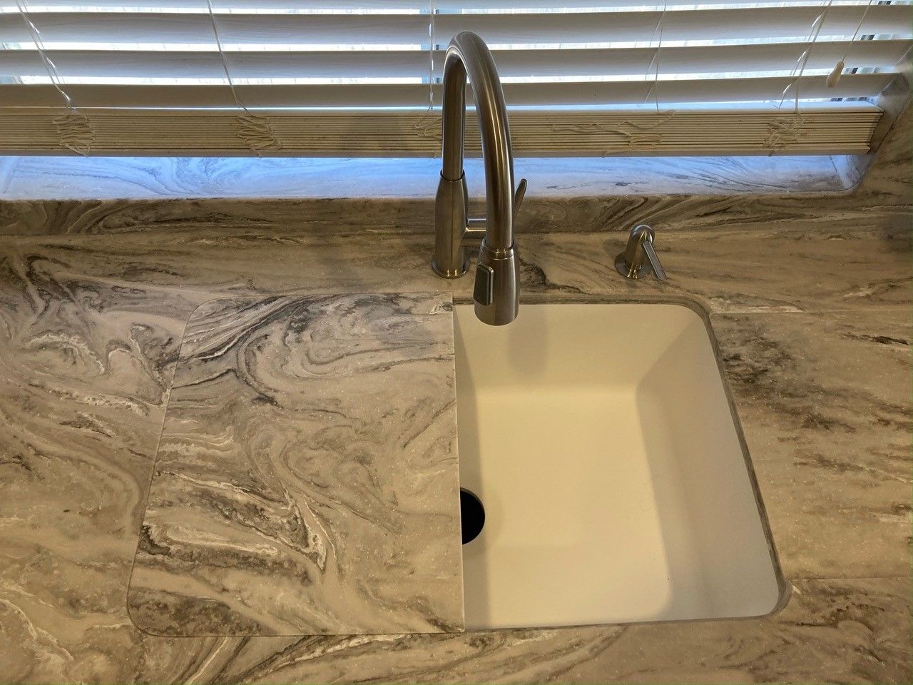 A kitchen sink with a faucet and a window in the background.