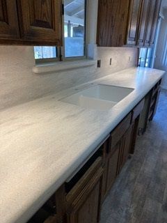 A kitchen with a sink , counter top , cabinets and a window.