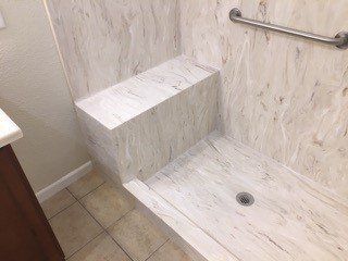 A bathroom with a walk in shower with a seat and a stainless steel railing.