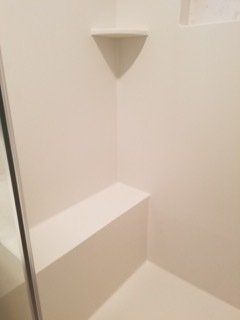 A shower with a bench and a shelf in it.