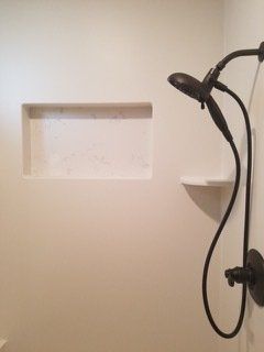 A bathroom with a shower head and a shelf.