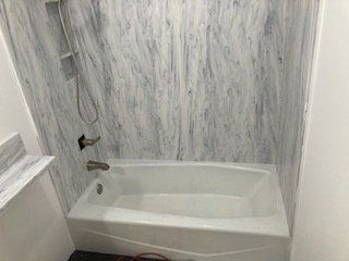 A bathtub in a bathroom with marble walls and a shower.
